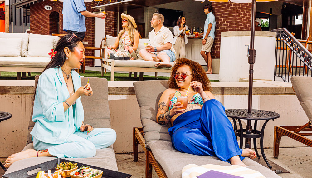 Two women with cocktails sit by the pool and chat at Kimpton Cottonwood Hotel