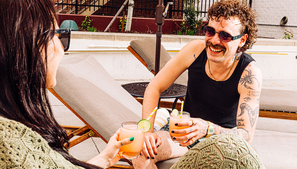 man and woman with cocktails sit by the pool and chat at Kimpton Cottonwood Hotel