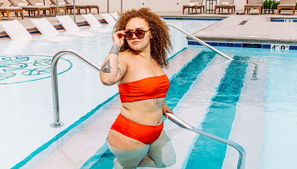 woman in orange two-piece bathing suit and sunglasses steps into the pool at Kimpton Cottonwood Hotel