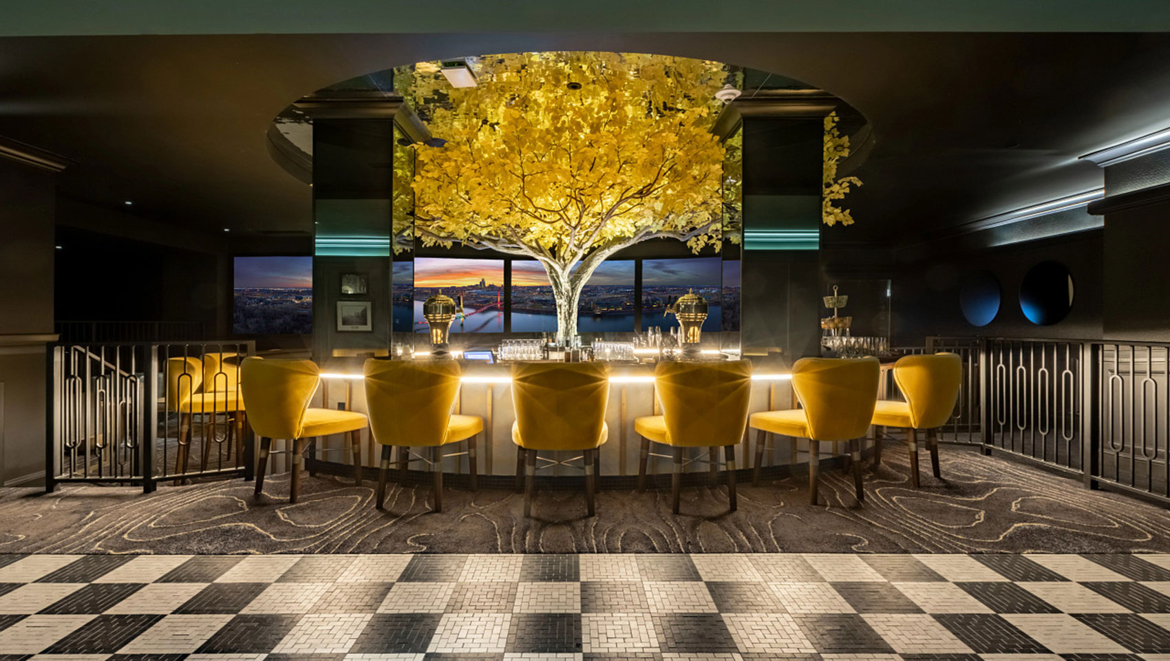 Committee Bar with lighted tree in center of bar which is surrounded by yellow bar chairs and an underlit bar