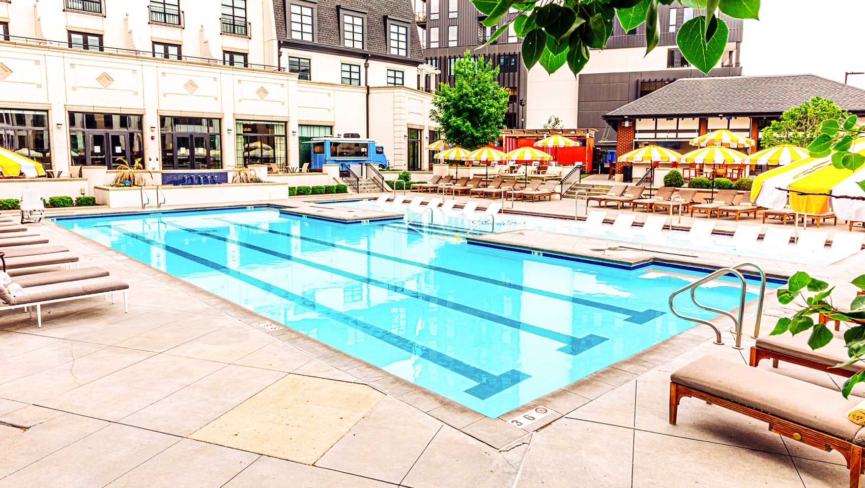The Cottonwood Hotel outdoor pool with lap lanes, in-water loungers, poolside chairs, and yellow-striped umbrellas surrounded by hotel buildings